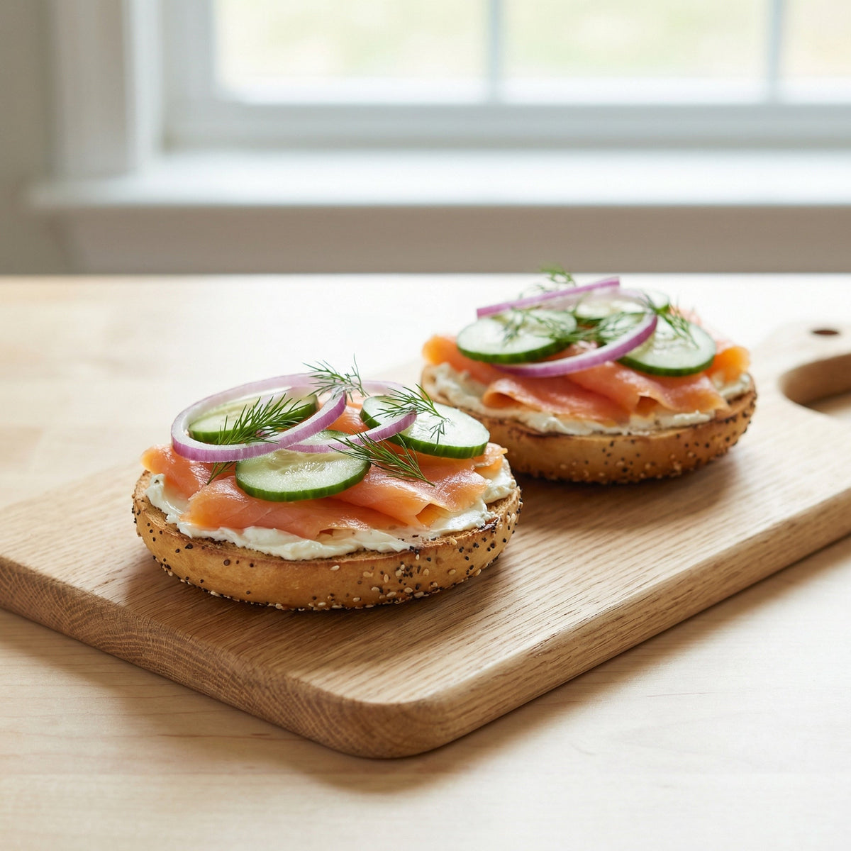 To bagelhalvdele med flødeost, røget laks, agurk, rødløg og dild på et træskærebræt